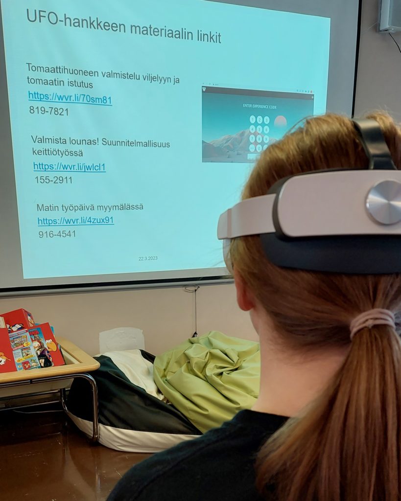 Henkilöllä on VR-lasit päässään. Taustalla on näyttö.