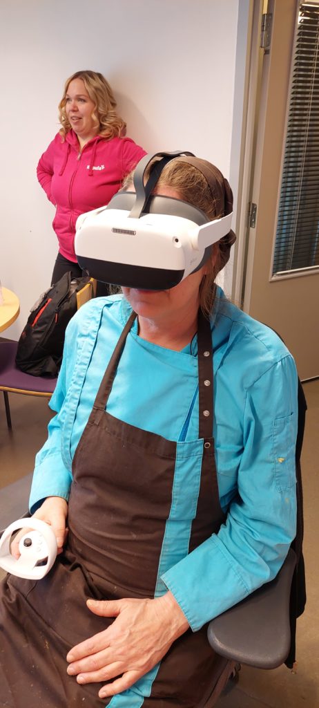 Henkilöllä on VR-lasit päässä. Toinen henkilö seisoo takana.