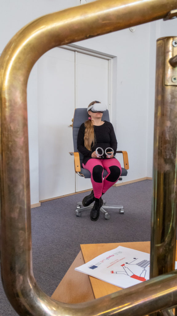 Henkilöllä on VR-lasit päässä ja hän istuu pyörivällä tuolilla.